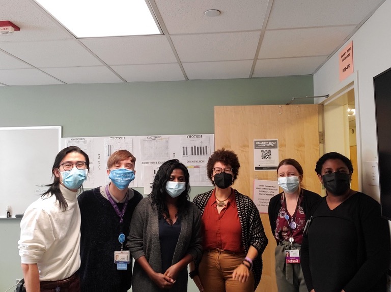 A group of 6 people standing together in a conference room, wearing masks and smiling. On the left is three residents, then Washington State Representative Kirsten Harris-Talley, and then on the right are two pathway leaders.